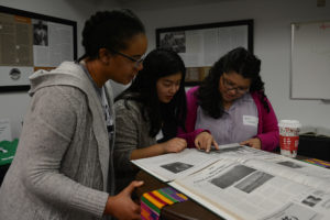 three women stand around table reading archive book